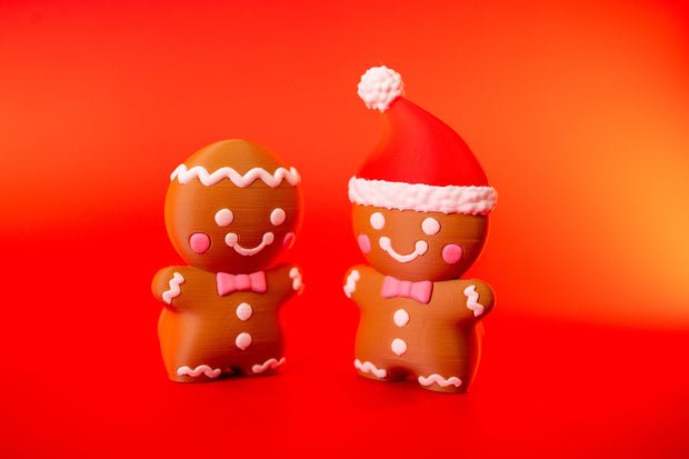 Two smiling gingerbread man Christmas fidgets, one with icing-style head trim and one wearing a Santa hat